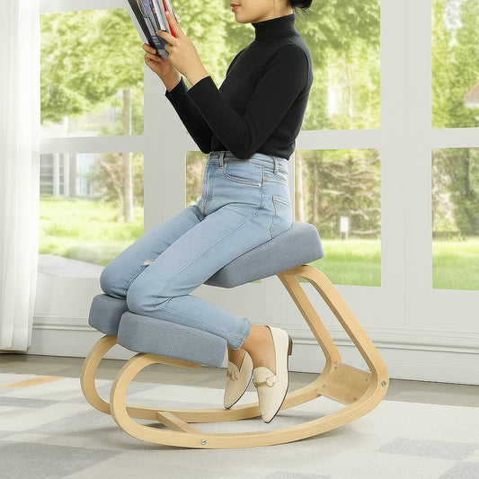 Person sitting on a wooden rocking chair reading a book in a bright room with large windows.